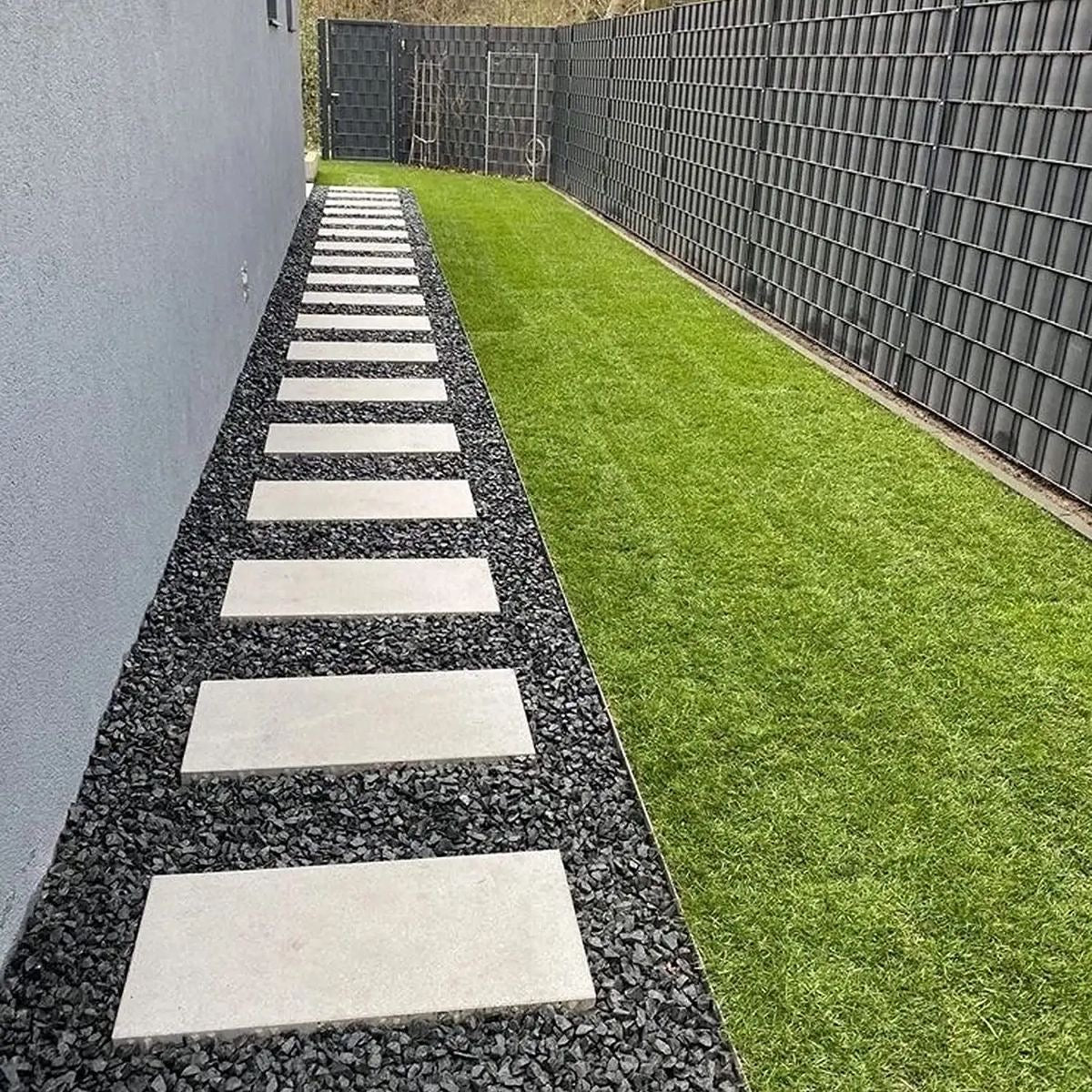 White porcelain tile path on black lava rock surrounded by green garden plants