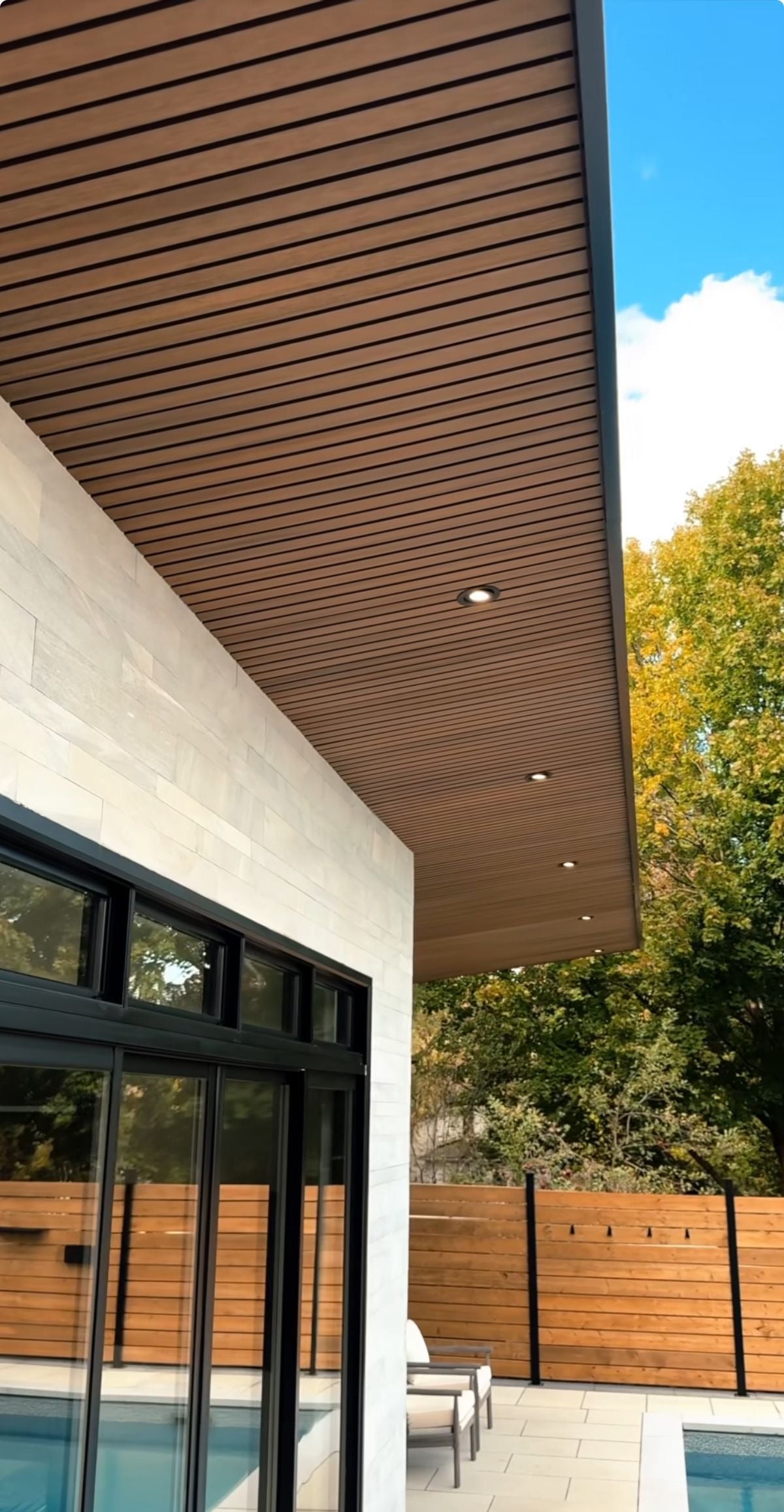 Exterior soffit ceiling with horizontal hardwood slats and recessed LED lighting over a pool deck